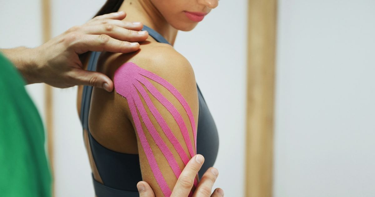 Physiotherapeut bringt ein elastisches kinesiologisches Tape auf der Schulter einer Patientin an