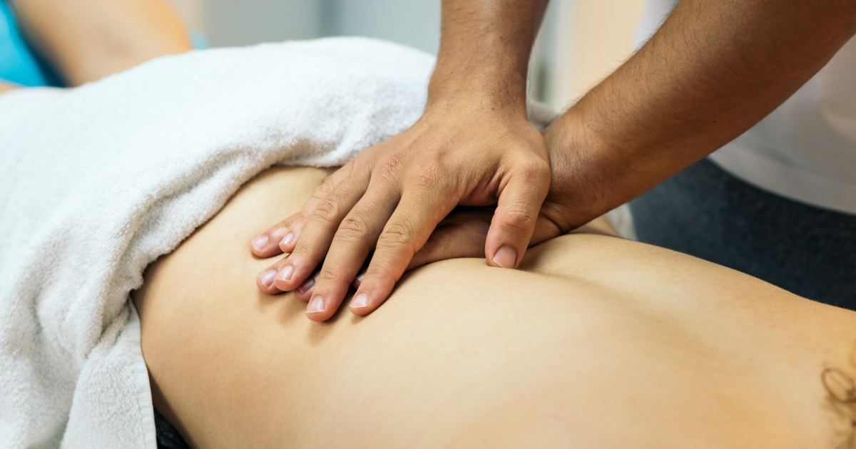 Therapeutin massiert den Rücken eines Patienten auf einer mobilen Massageliege